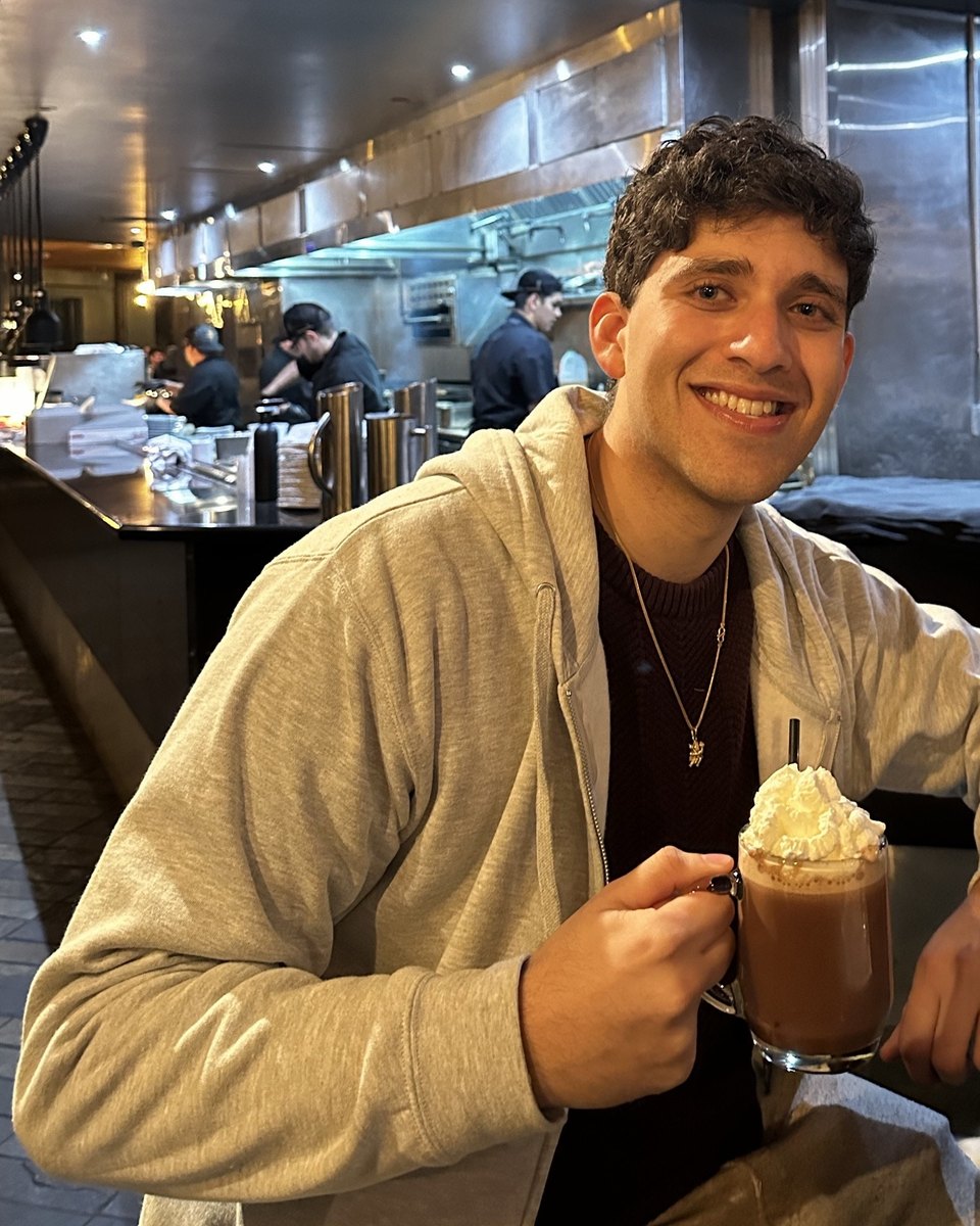 Aakash smiling at a counter with a mug of hot chocolate
